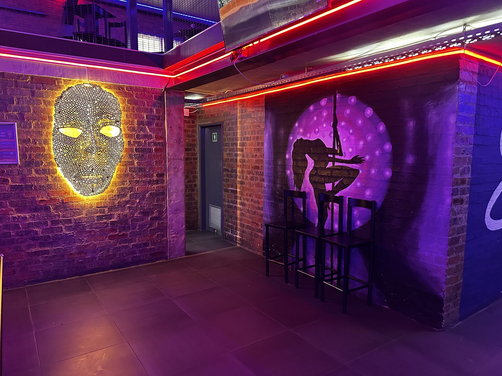 Entrance passage with lit mask artwork and pole dancer mural at Cheeky Tiger Midrand
