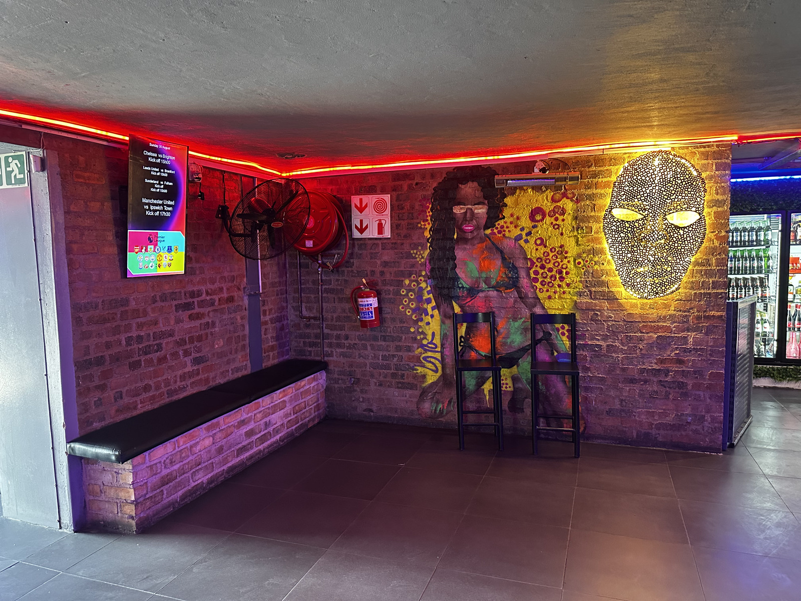 Glowing mask artwork and painted mural beside the fixtures counter at Cheeky Tiger Midrand