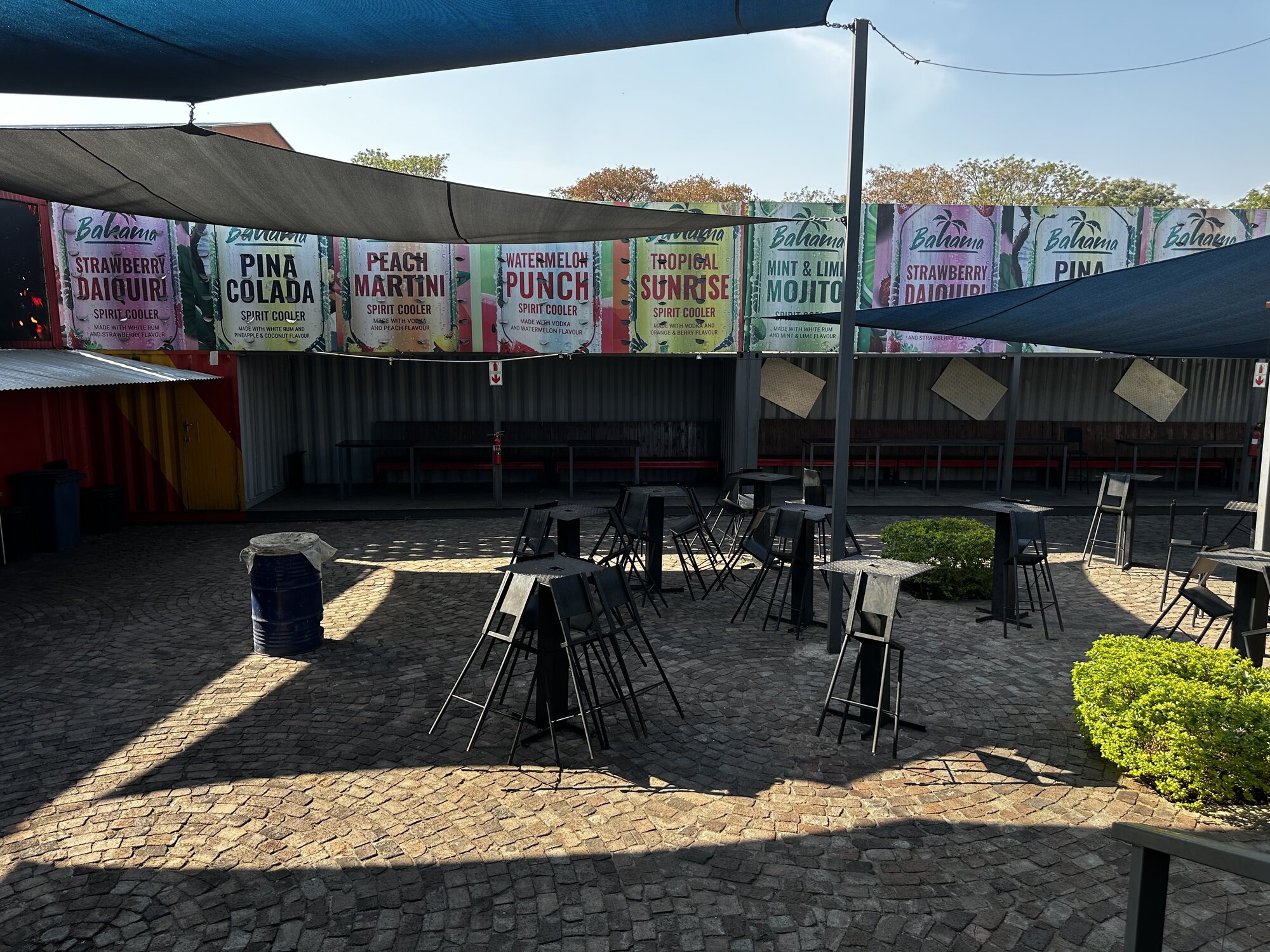 Outside courtyard with shade sails, cobbles and cocktail banners at Cheeky Tiger Midrand