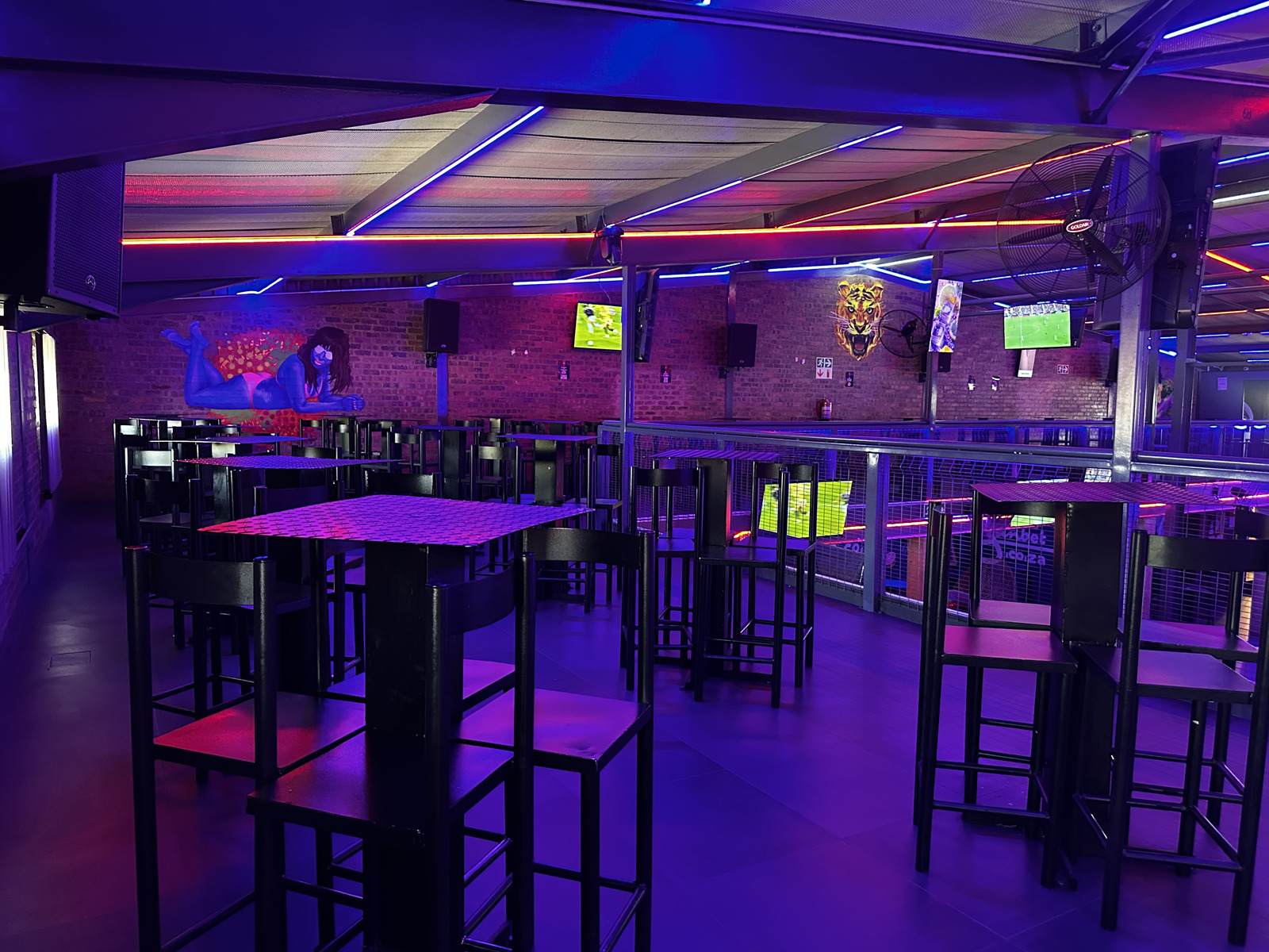 Upper deck high tables and bar stools under blue neon at Cheeky Tiger Midrand