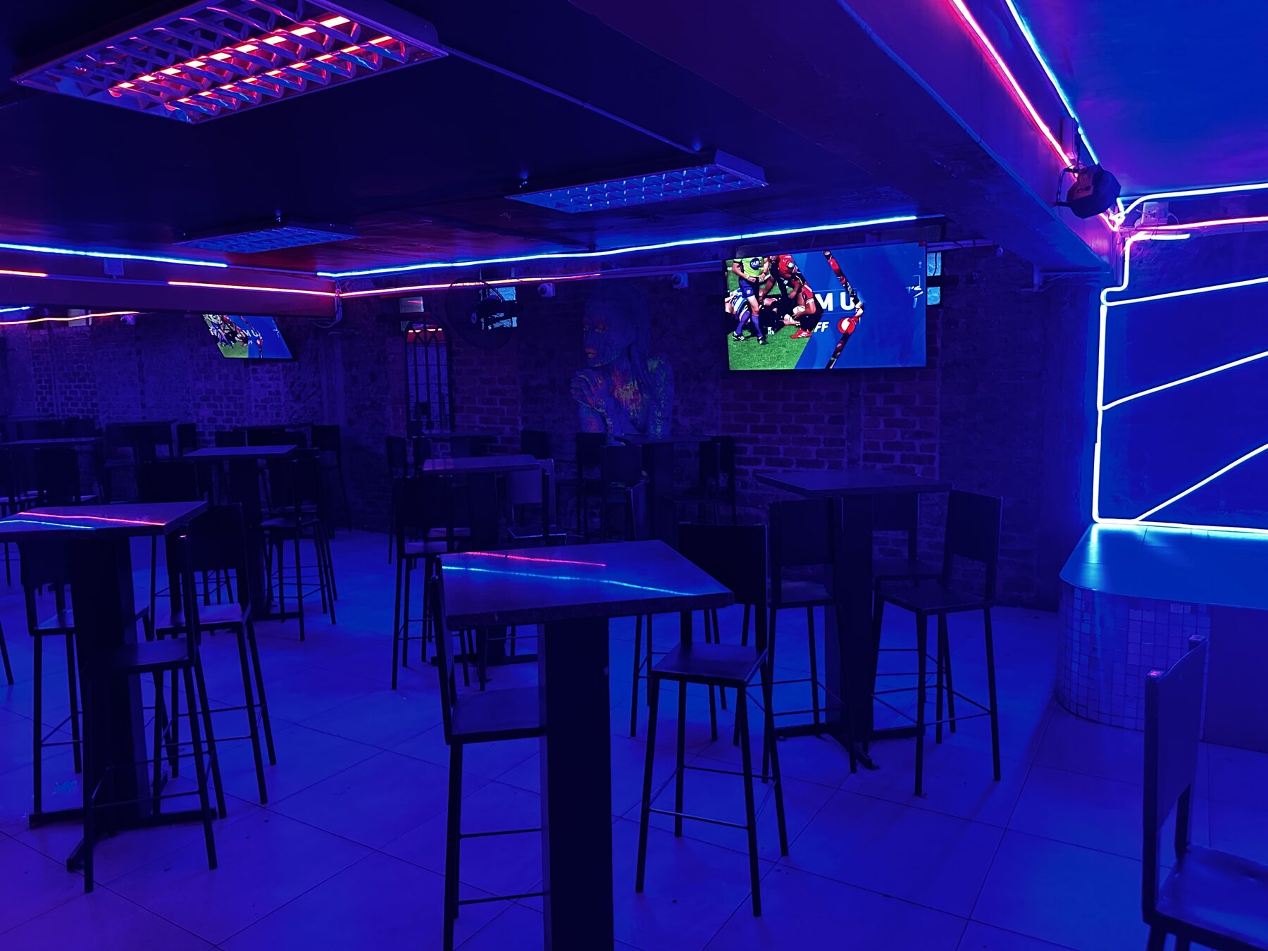 High tables and bar stools under blue and pink neon strip lighting at Cheeky Tiger Diepkloof Hotel